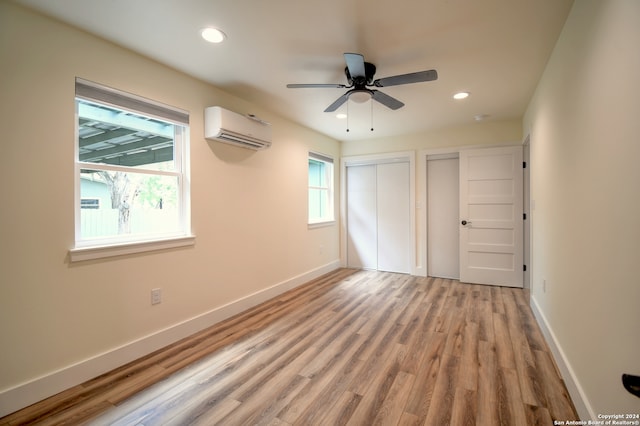 unfurnished bedroom featuring wood-type flooring, ceiling fan, two closets, and a wall mounted air conditioner