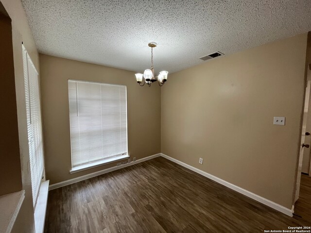 unfurnished room featuring a textured ceiling, dark wood-type flooring, and a notable chandelier