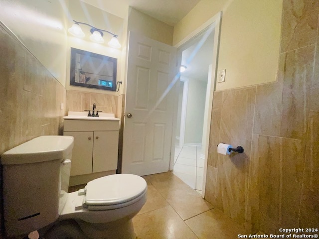 bathroom with vanity, toilet, tile flooring, and tile walls