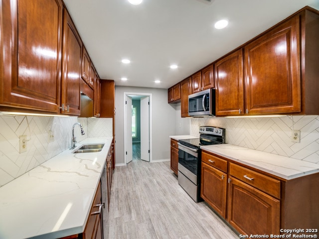 kitchen featuring sink, tasteful backsplash, stainless steel appliances, light hardwood / wood-style flooring, and light stone countertops