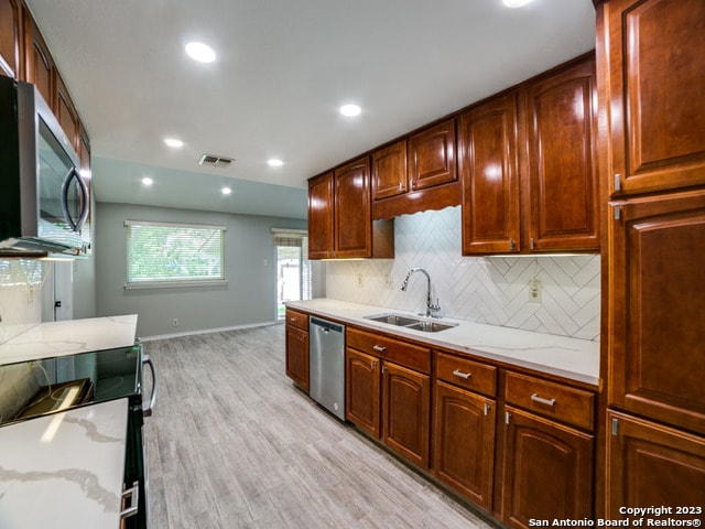 kitchen with appliances with stainless steel finishes, sink, light hardwood / wood-style floors, backsplash, and light stone countertops