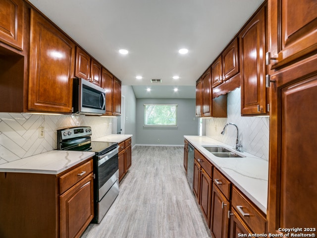 kitchen with light stone counters, appliances with stainless steel finishes, sink, light hardwood / wood-style floors, and tasteful backsplash