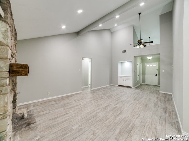 empty room featuring high vaulted ceiling, a stone fireplace, ceiling fan, light hardwood / wood-style floors, and beam ceiling