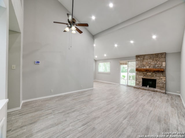 unfurnished living room with high vaulted ceiling, a fireplace, light hardwood / wood-style flooring, and ceiling fan