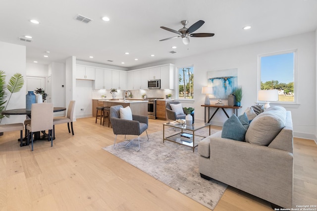 living room featuring ceiling fan, sink, and light hardwood / wood-style flooring