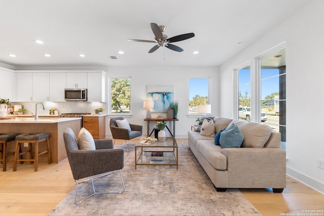 living room featuring ceiling fan, sink, and light wood-type flooring