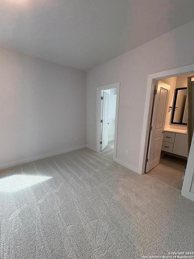 unfurnished bedroom featuring light carpet and ensuite bathroom