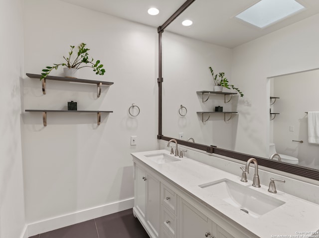 bathroom with a skylight, tile patterned flooring, toilet, and dual bowl vanity