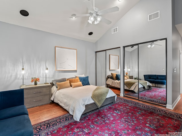 bedroom with multiple closets, ceiling fan, light hardwood / wood-style flooring, and high vaulted ceiling