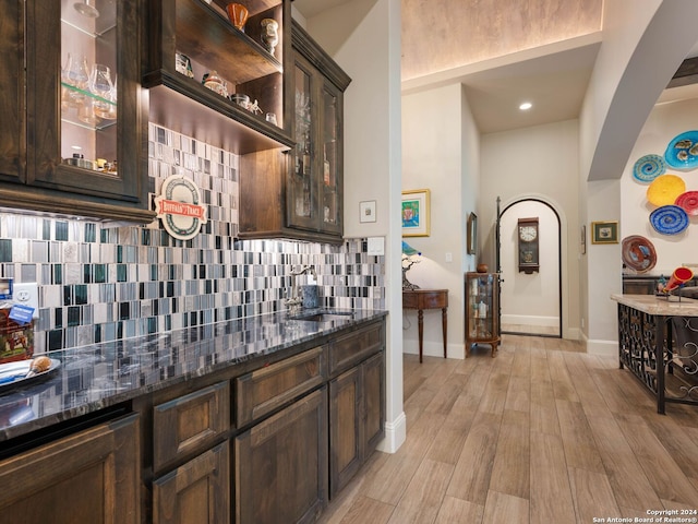 kitchen featuring dark brown cabinets, sink, tasteful backsplash, dark stone counters, and light hardwood / wood-style floors