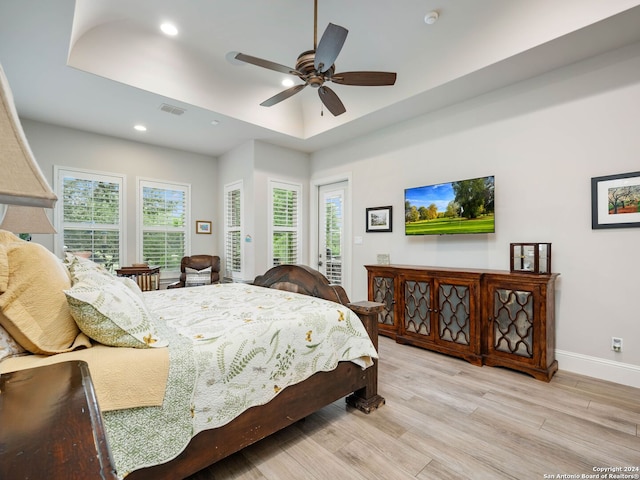 bedroom featuring ceiling fan, light wood-type flooring, access to exterior, and a tray ceiling