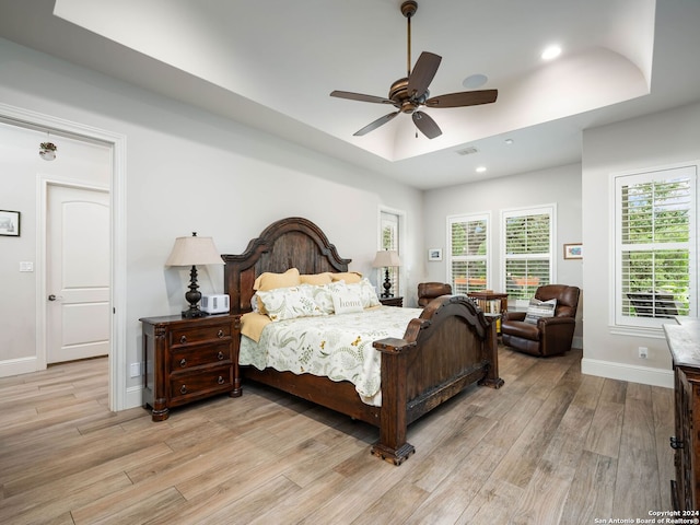 bedroom with a raised ceiling, ceiling fan, and light hardwood / wood-style floors