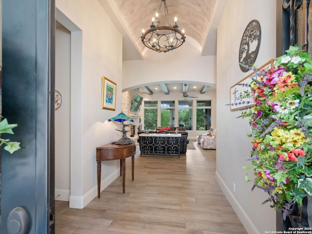 entryway with ceiling fan with notable chandelier, beam ceiling, high vaulted ceiling, and hardwood / wood-style flooring