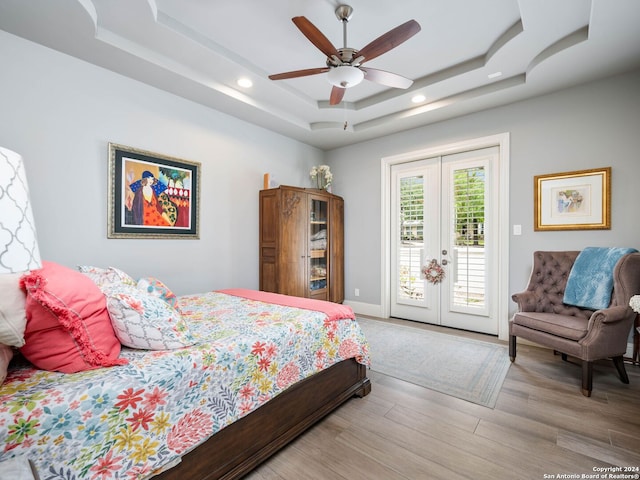 bedroom with french doors, ceiling fan, access to exterior, a tray ceiling, and hardwood / wood-style flooring