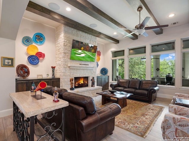 living room featuring a stone fireplace, beamed ceiling, ceiling fan, and hardwood / wood-style flooring