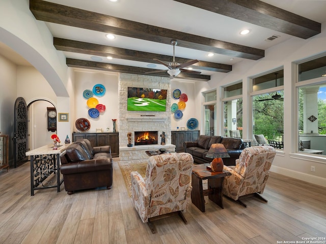 living room with wood-type flooring, beam ceiling, ceiling fan, and a stone fireplace