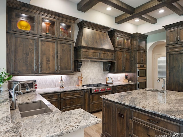 kitchen with custom exhaust hood, sink, backsplash, light wood-type flooring, and stainless steel appliances