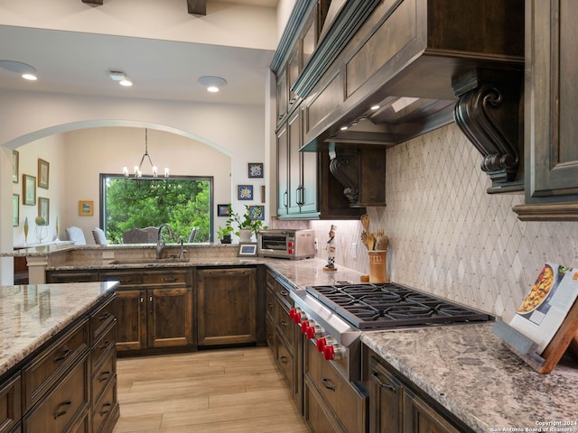 kitchen featuring tasteful backsplash, light stone counters, sink, a notable chandelier, and light wood-type flooring