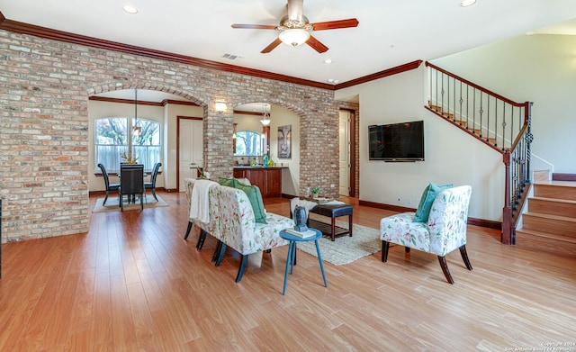 living room with brick wall, ornamental molding, ceiling fan, and light wood-type flooring