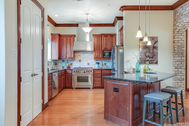 kitchen with appliances with stainless steel finishes, wall chimney exhaust hood, tasteful backsplash, light wood-type flooring, and pendant lighting