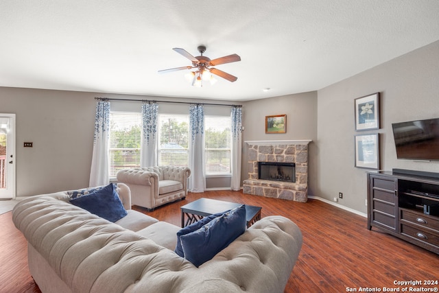 living room with a stone fireplace, wood-type flooring, and ceiling fan