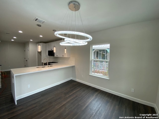 kitchen with white cabinets, dark wood-type flooring, kitchen peninsula, and backsplash