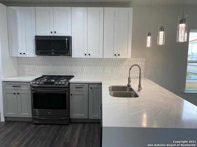 kitchen featuring decorative light fixtures, black gas range oven, dark wood-type flooring, sink, and tasteful backsplash