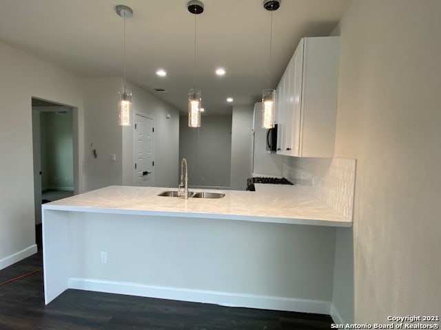 kitchen with kitchen peninsula, dark wood-type flooring, white cabinets, and sink