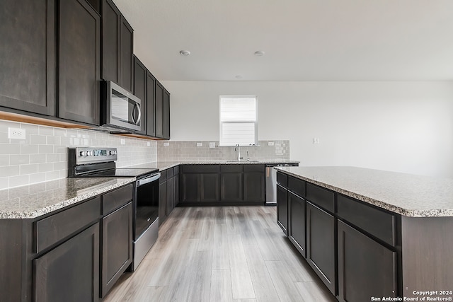 kitchen featuring sink, dark brown cabinets, stainless steel appliances, light hardwood / wood-style floors, and decorative backsplash