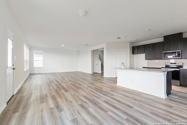 kitchen with tasteful backsplash, stainless steel appliances, a center island, light stone countertops, and light hardwood / wood-style floors