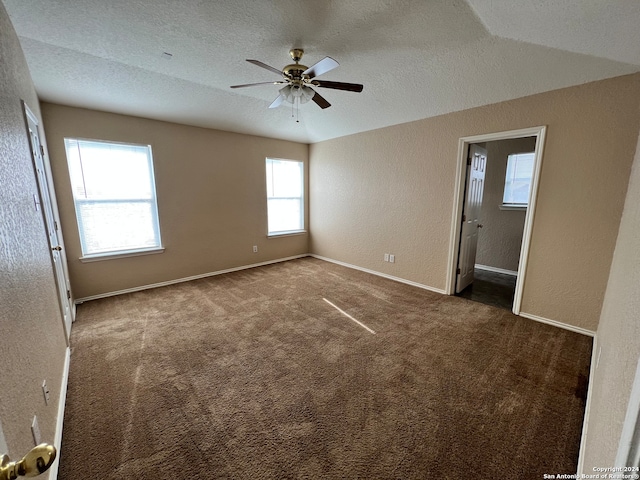 carpeted spare room featuring a textured ceiling, vaulted ceiling, ceiling fan, and plenty of natural light