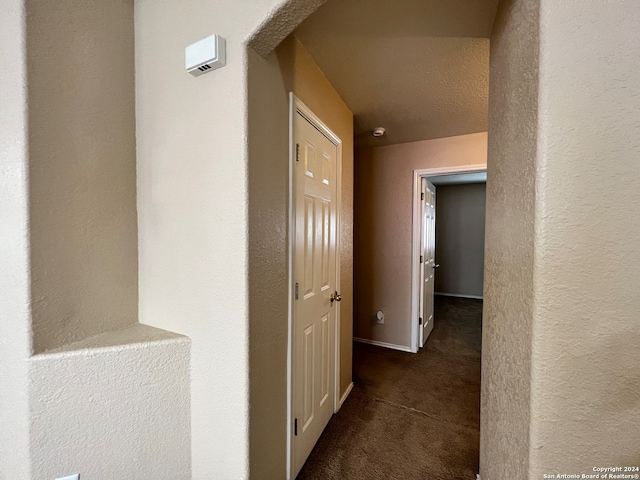 hallway with dark carpet and a textured ceiling