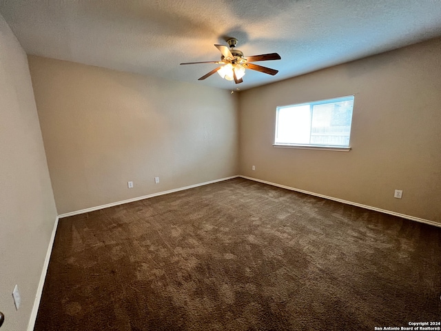 empty room featuring a textured ceiling, dark colored carpet, and ceiling fan