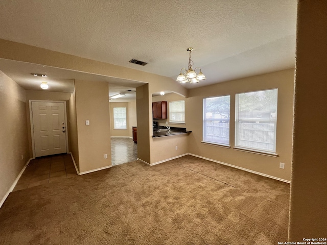 unfurnished living room featuring a textured ceiling, carpet flooring, and a notable chandelier