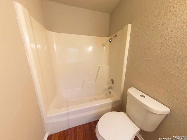 bathroom featuring hardwood / wood-style floors, washtub / shower combination, toilet, and a textured ceiling