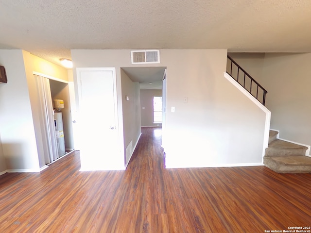 empty room with dark hardwood / wood-style floors, water heater, and a textured ceiling