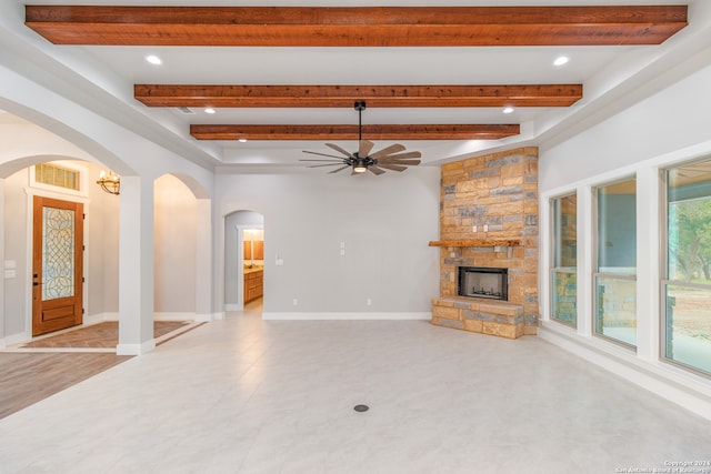 unfurnished living room featuring beam ceiling, ceiling fan, a fireplace, and light tile floors