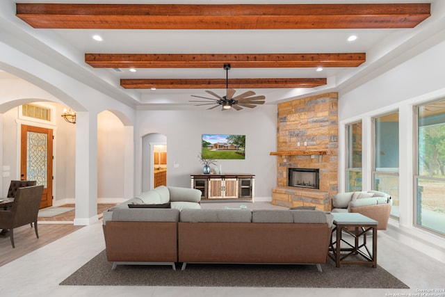 living room featuring light wood-type flooring, beam ceiling, ceiling fan, and a stone fireplace