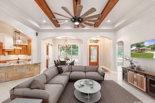 tiled living room featuring beamed ceiling, sink, and ceiling fan with notable chandelier