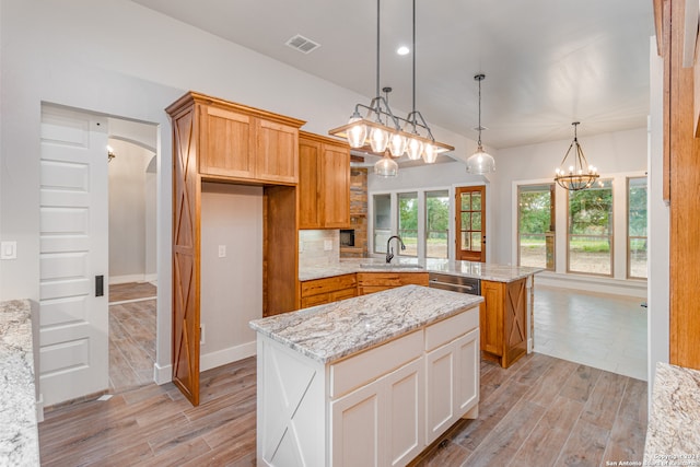 kitchen featuring hanging light fixtures, light hardwood / wood-style floors, tasteful backsplash, light stone counters, and sink