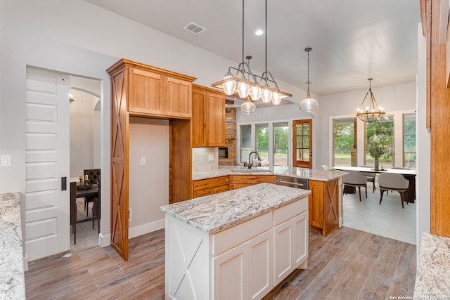 kitchen with light stone countertops, hanging light fixtures, backsplash, sink, and a center island