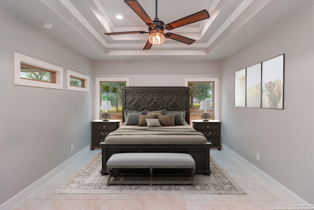 bedroom with ceiling fan, a tray ceiling, light tile flooring, and multiple windows