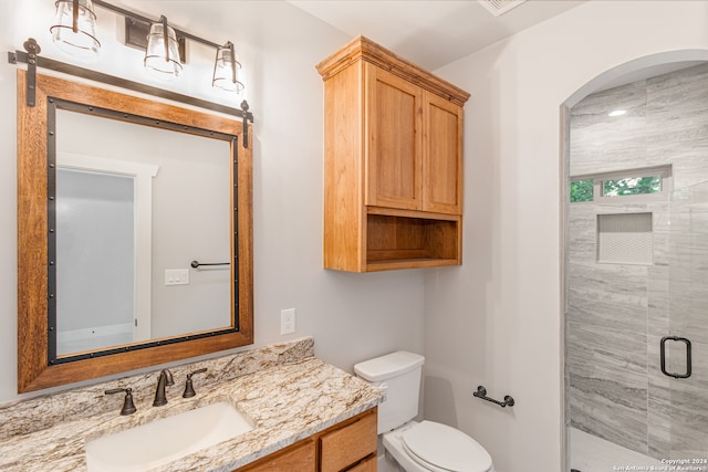 bathroom featuring a shower with door, vanity, and toilet