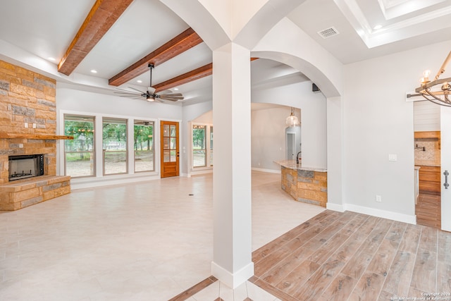 unfurnished living room featuring tile flooring, ceiling fan with notable chandelier, beam ceiling, a skylight, and a fireplace