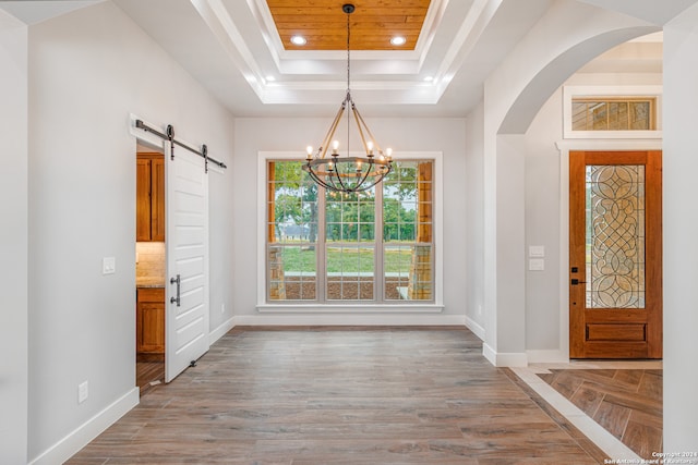 foyer entrance featuring a raised ceiling, a chandelier, and a barn door