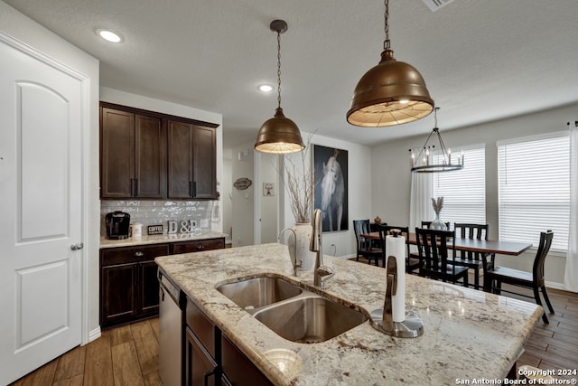 kitchen with light stone countertops, tasteful backsplash, a center island with sink, decorative light fixtures, and dark wood-type flooring