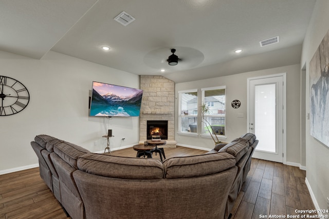 living room with a stone fireplace, dark hardwood / wood-style floors, and ceiling fan