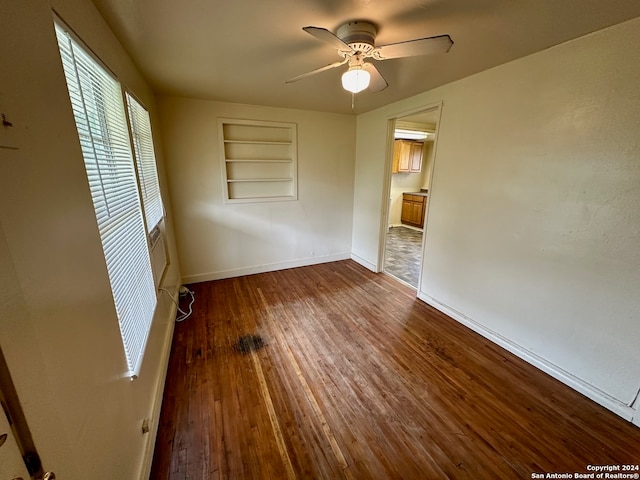 unfurnished room with built in features, dark wood-type flooring, and ceiling fan