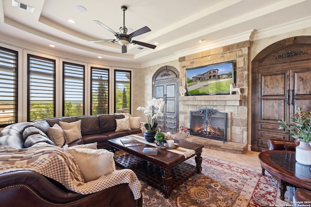 tiled living room featuring plenty of natural light, a fireplace, ceiling fan, and a tray ceiling