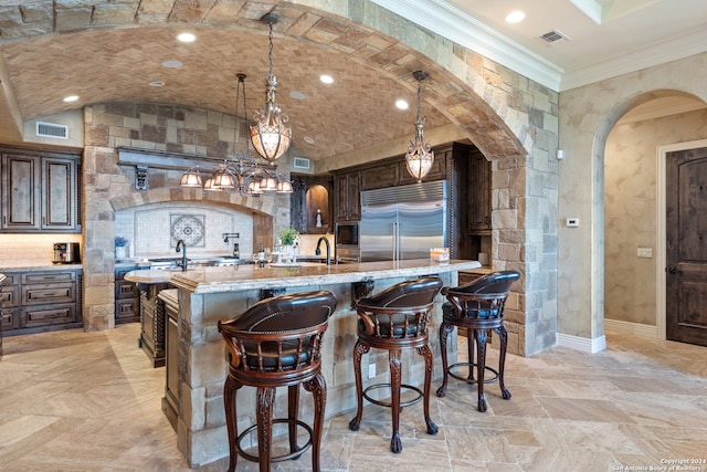 kitchen featuring built in appliances, dark brown cabinets, light stone counters, a kitchen breakfast bar, and pendant lighting